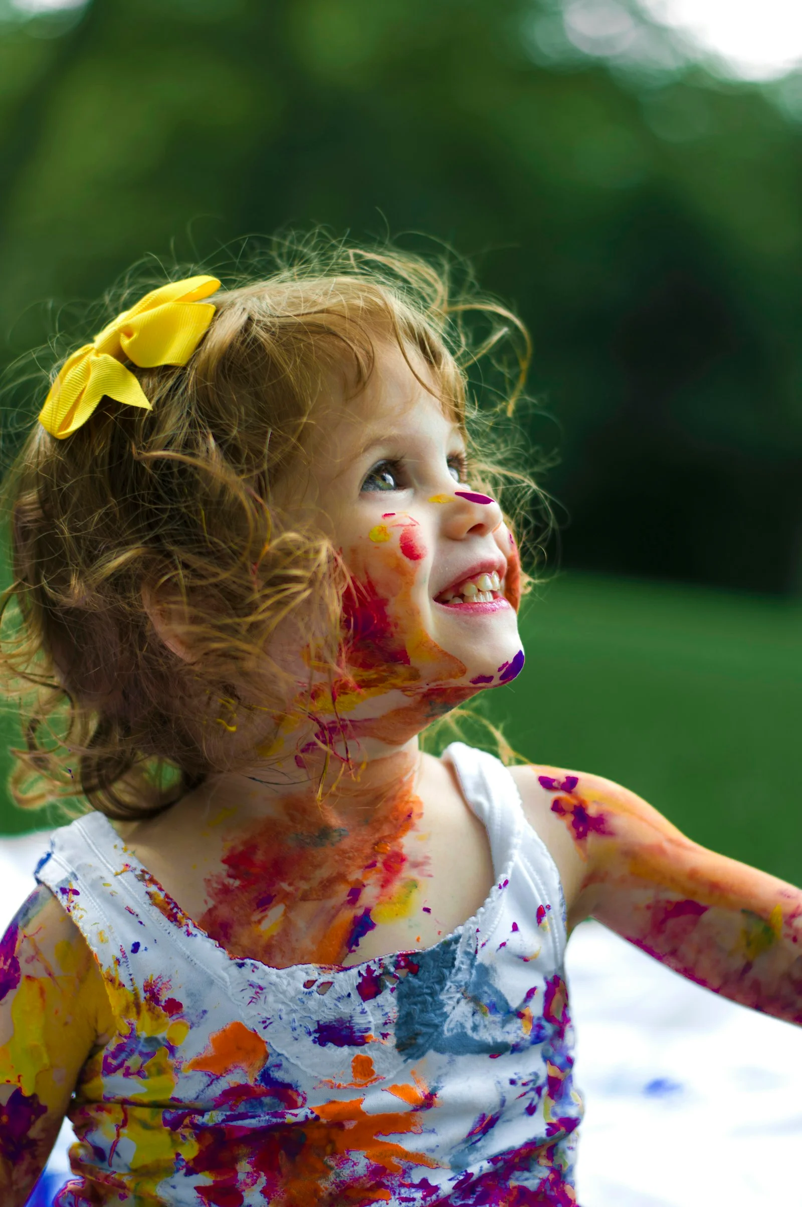 A smiling child with colourful paint on their face and clothes
